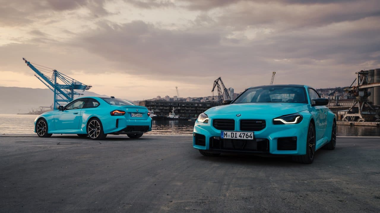 Two M2 xDrive models in Zandvoort Blue at a harbour, showing front and rear perspectives.