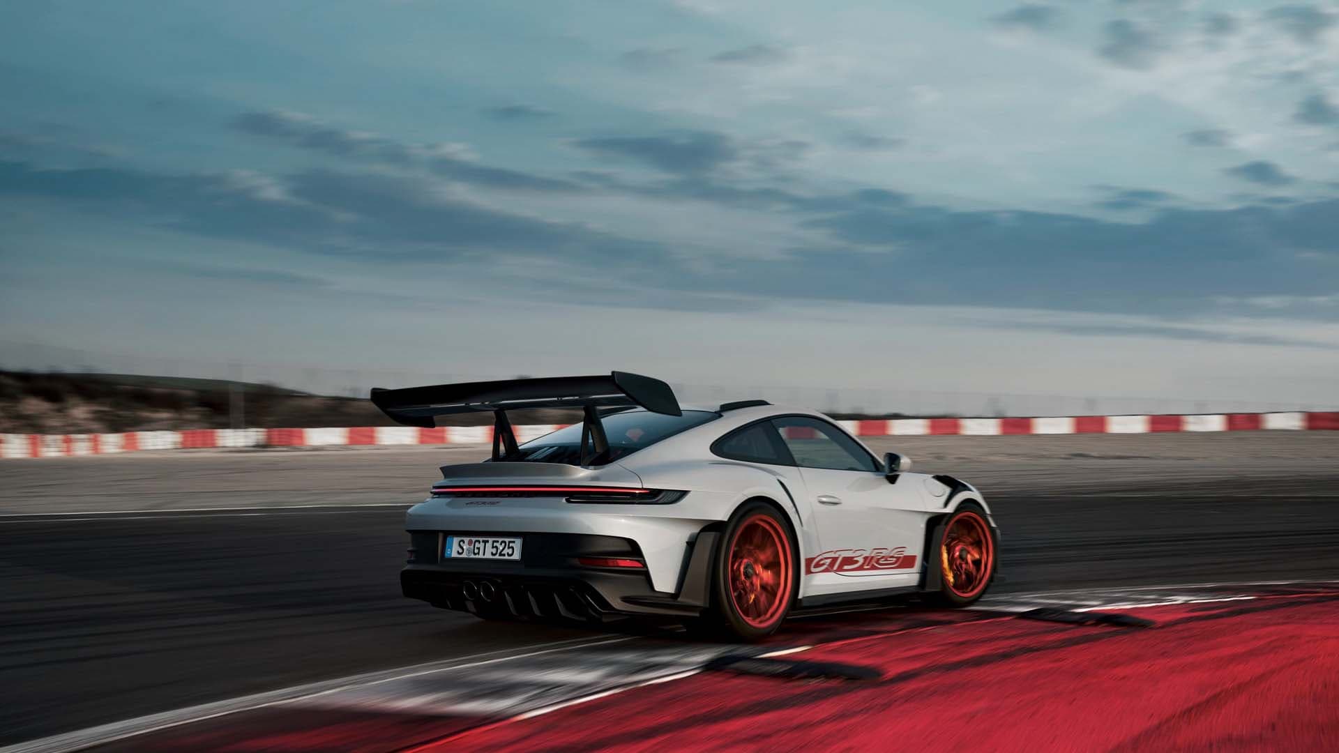 992 GT3 RS at speed on track, rear three-quarter view showing the swan-neck rear wing and diffuser.